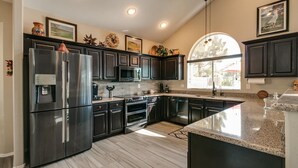 A modern kitchen with dark cabinetry, stainless steel appliances, and a large window providing natural light. - Spectacular Golf Course Home With Pool and Views! (Gilbert)