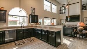 A modern kitchen with dark cabinets, a stainless steel dishwasher, a large island, and a ceiling fan. - Spectacular Golf Course Home With Pool and Views! (Gilbert)