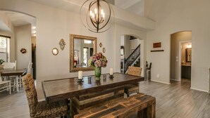 A dining area with a dark wooden table, wicker chairs, a bench, a chandelier, and a large mirror on the wall. - Spectacular Golf Course Home With Pool and Views! (Gilbert)