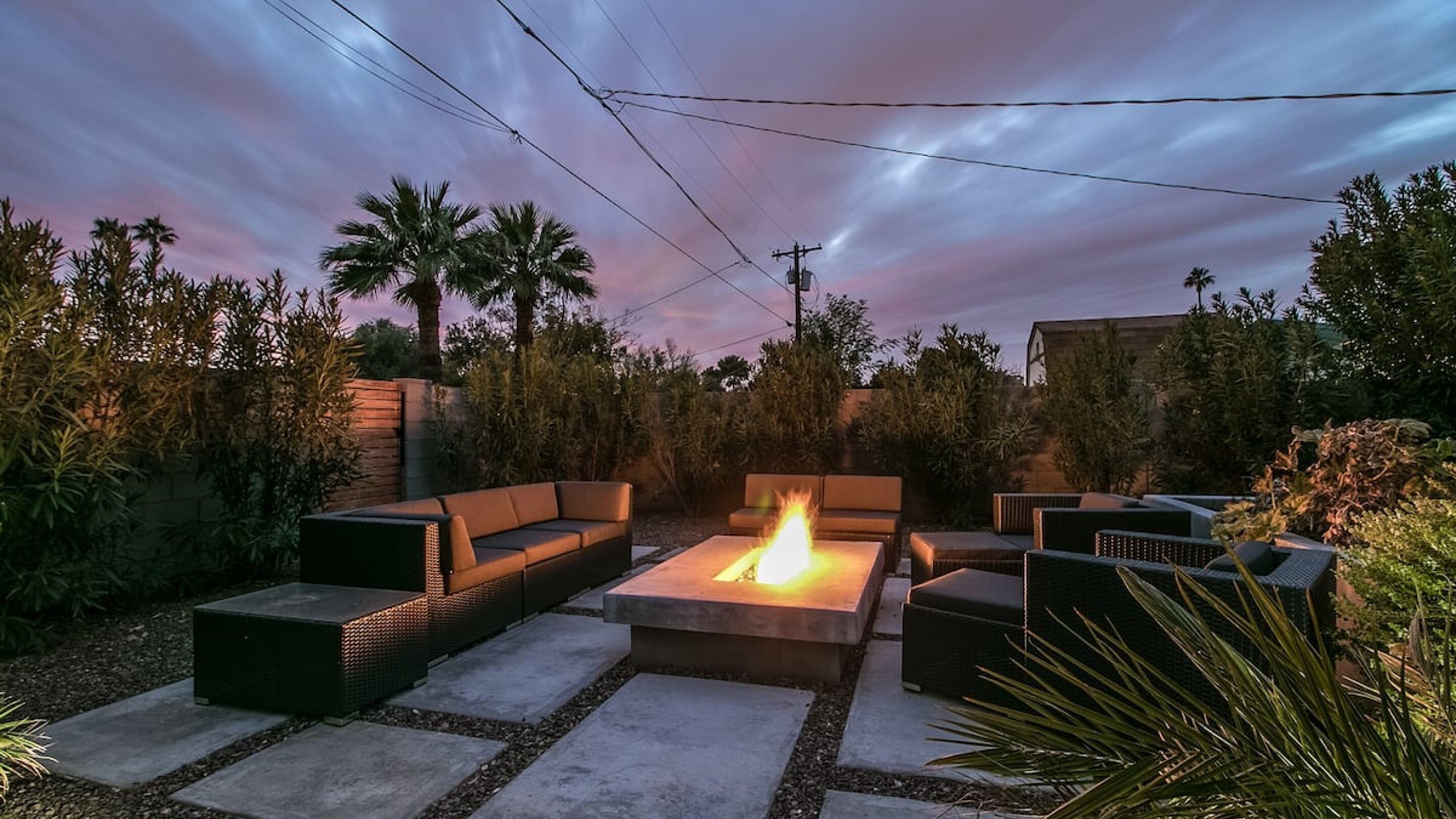 An outdoor patio with a fire pit, seating area, and surrounding vegetation.