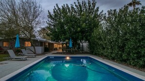 A swimming pool with lounge chairs and umbrellas, surrounded by trees and a house with a patio. - Mid-century Modern W/backyard Oasis, Putting Green (Phoenix)