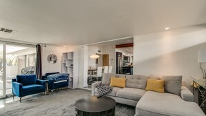 A modern living room with a grey sofa, a blue armchair, and a coffee table. There is a dining area with a table and chairs visible through an open door. - Mid-century Modern W/backyard Oasis, Putting Green (Phoenix)