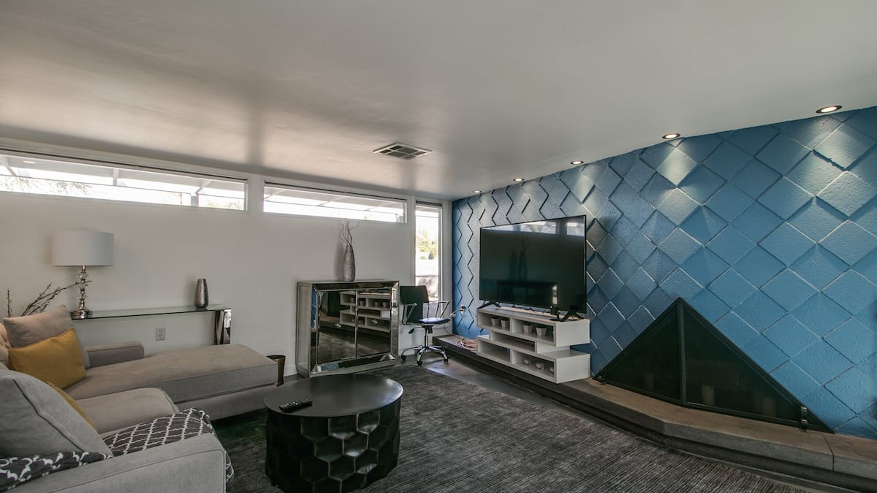 Een moderne woonkamer met een grote televisie, een open haard en een blauwe muur met structuur.