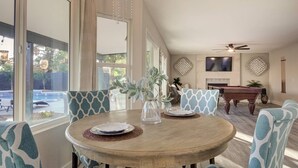 A dining area with a round wooden table, patterned chairs, a vase with greenery, and a pool visible through the window. - Scottsdale Kierland 4 Bdrm W/resort Like Backyard (Scottsdale)