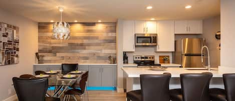 A modern kitchen with a central island, stainless steel appliances, and a dining area with chairs and a table.