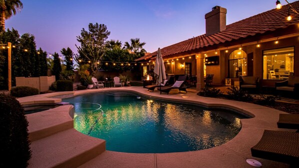 A swimming pool with steps leading into it, surrounded by lounge chairs and a patio area with string lights. - Luxury N. Scottsdale Home W/private Oasis Yard! (Scottsdale)
