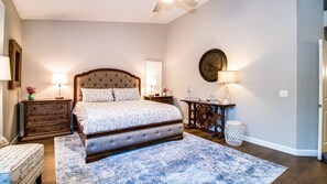 A bedroom with a large bed, wooden headboard, two bedside tables with lamps, a round wall clock, and a small white trash bin. - Luxury N. Scottsdale Home W/private Oasis Yard! (Scottsdale)