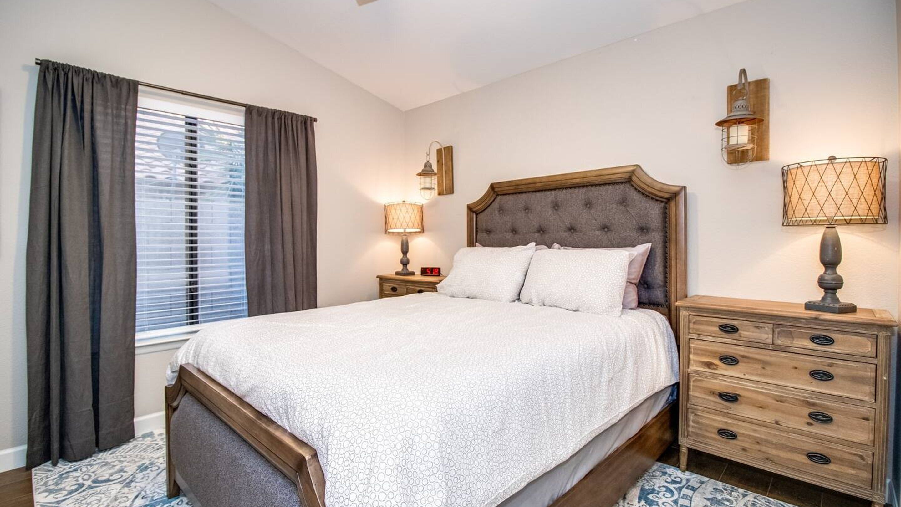 Une chambre à coucher avec un grand lit, une table de chevet avec une lampe, une commode et une fenêtre avec des rideaux.