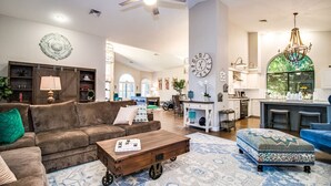 Un salon spacieux avec un canapé marron, une table basse en bois et un tapis à motifs. On y trouve également un coin cuisine avec des placards blancs et une grande fenêtre.