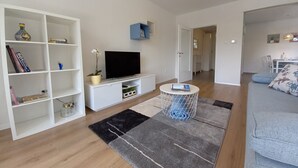En stue med fjernsyn, hvide hylder, et rundt sofabord og en sofa.