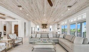 A spacious living area with a large sectional sofa, a glass coffee table, and a wooden ceiling.