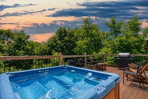 A hot tub on a wooden deck with a view of trees and a cloudy sky.