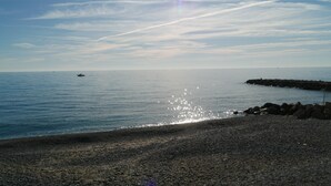 A beach with a rocky shoreline, calm water, and a distant boat. - Vista Mare (Menton)