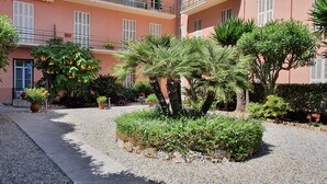 A courtyard with a gravel path, potted plants, and a building with balconies and windows. - Vista Mare (Menton)