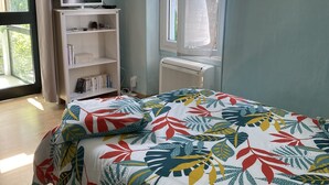 Ein Schlafzimmer mit Bett, Fernseher, Bücherregal, einem Fenster mit Vorhängen und einer Heizung.