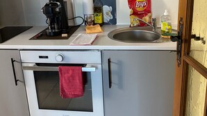 Eine kleine Küche mit Kaffeemaschine, Olivenölflasche, einer Tüte Lay's Chips, Spülmittel und einem kleinen Handtuch auf der Arbeitsfläche.