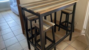 Eine Küche mit Holztisch, Hockern, einem Heizkörper und einem Fenster mit Vorhängen.