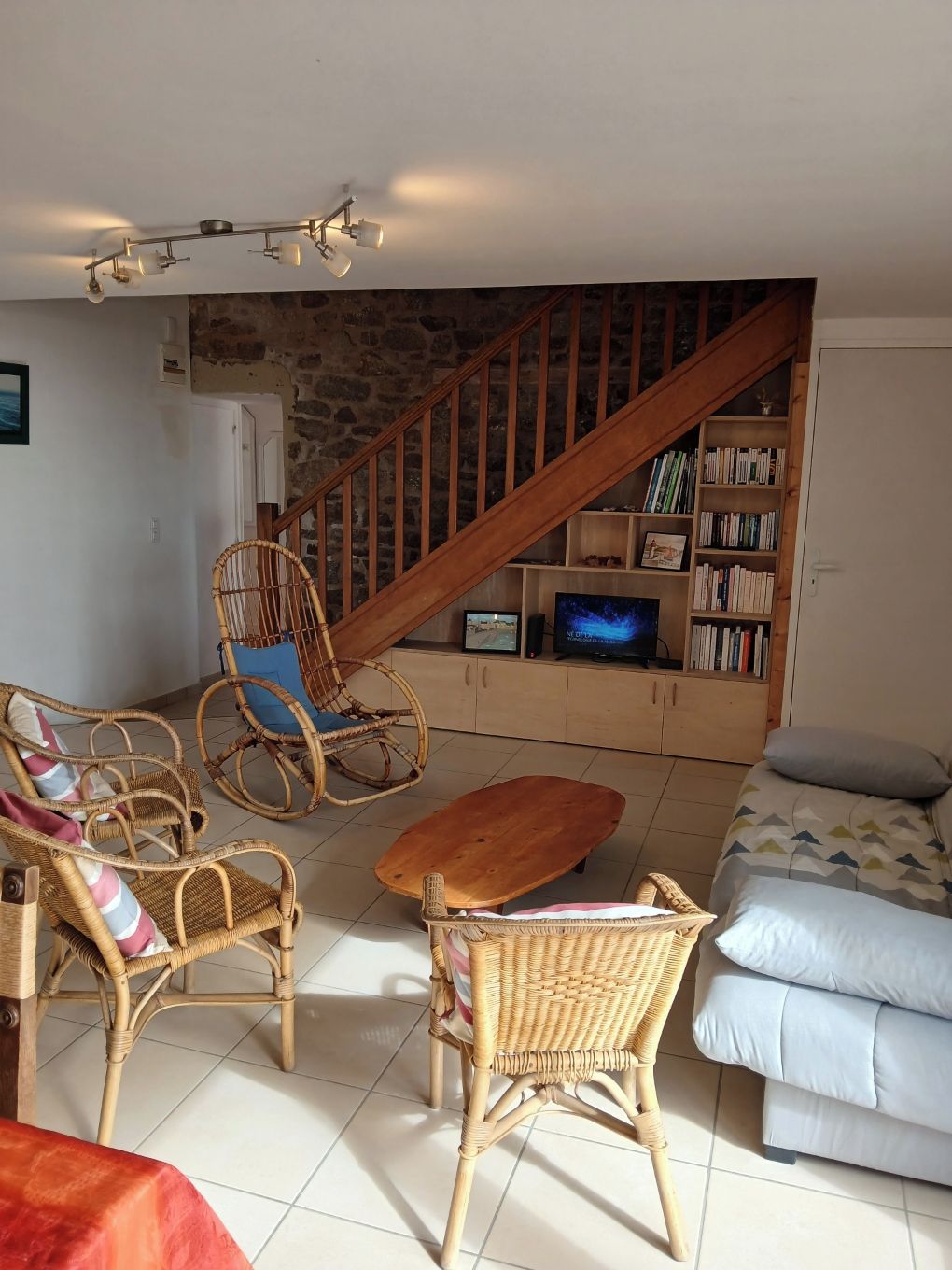 A living room with wicker furniture, a wooden staircase, a television, and a bookshelf.