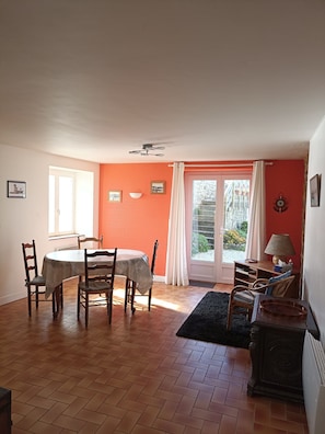 Een eetgedeelte met een tafel en stoelen, een bank, een lamp en uitzicht door een raam.
