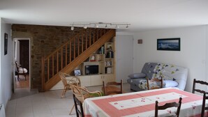 Ein gemütliches Wohnzimmer mit einer Holztreppe, einer Couch, einem Esstisch mit Stühlen und einem Bücherregal.