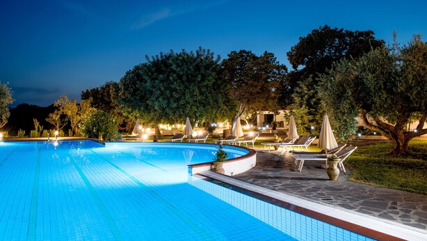 Ein Schwimmbecken mit Liegestühlen und Sonnenschirmen, umgeben von Bäumen und Steinwegen.