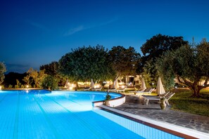 Ein Schwimmbecken mit Liegestühlen und Sonnenschirmen, umgeben von Bäumen und Steinwegen.