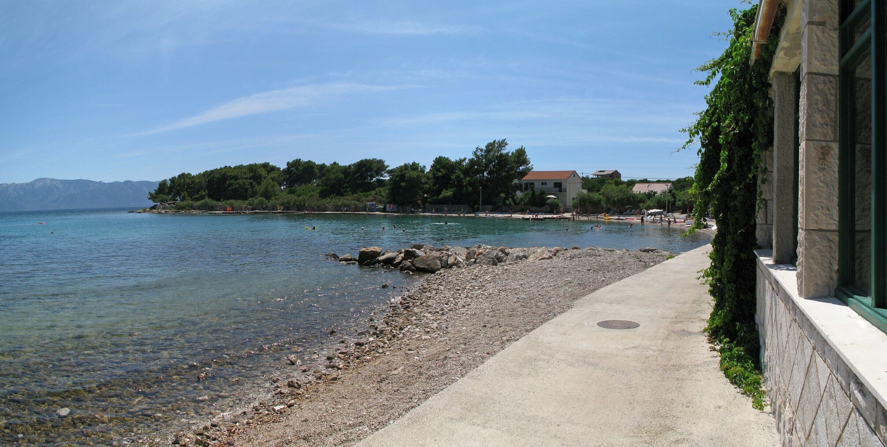 Une promenade en bord de mer offrant une vue dégagée sur la mer et les montagnes lointaines.