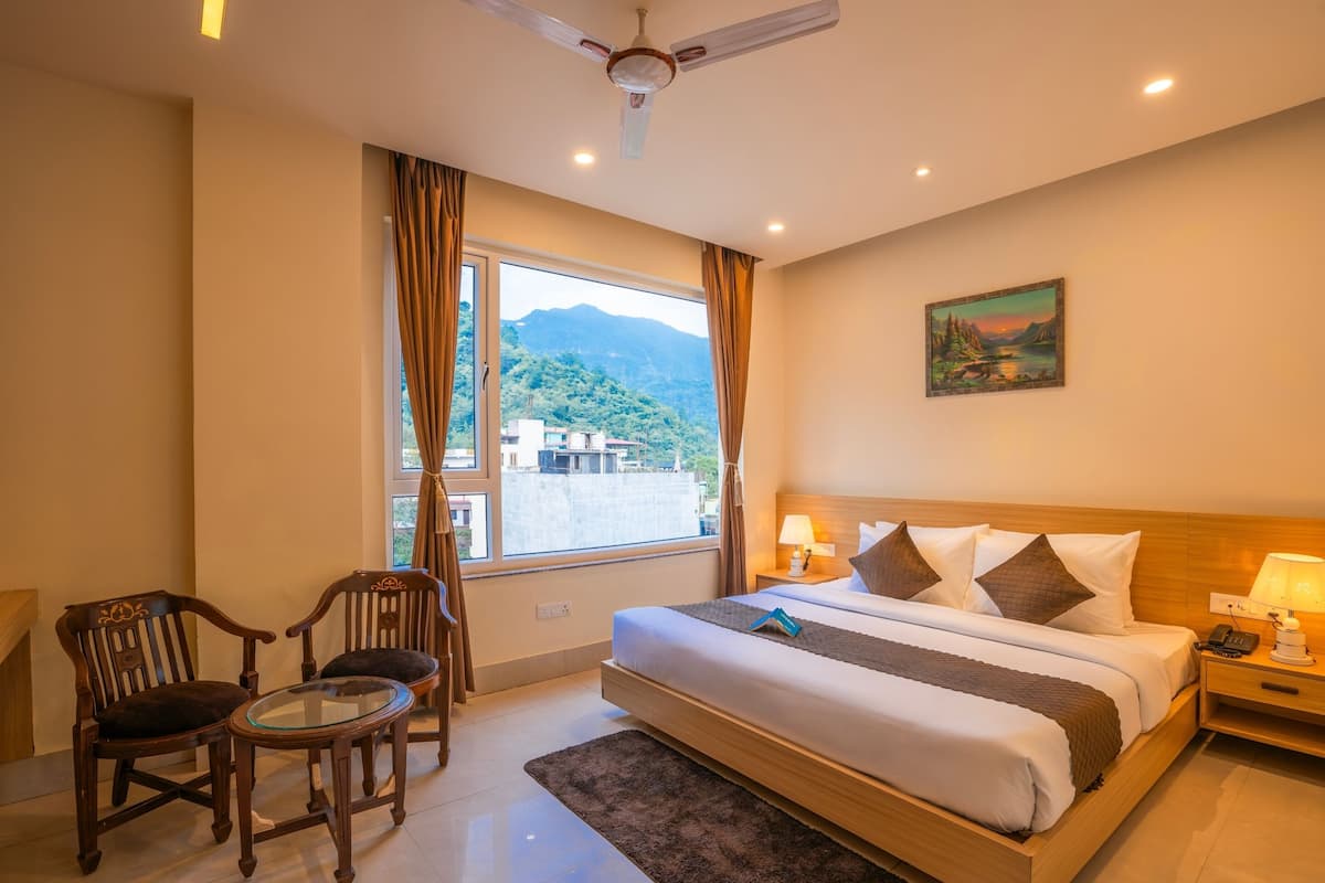 A hotel room with a bed, two chairs, a small table, a nightstand with a lamp, and a painting on the wall.