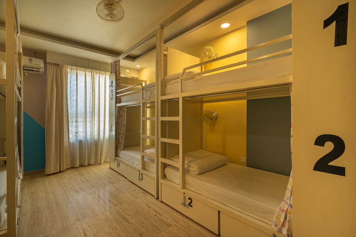 A dormitory room with bunk beds, numbered doors, and a window with curtains.
