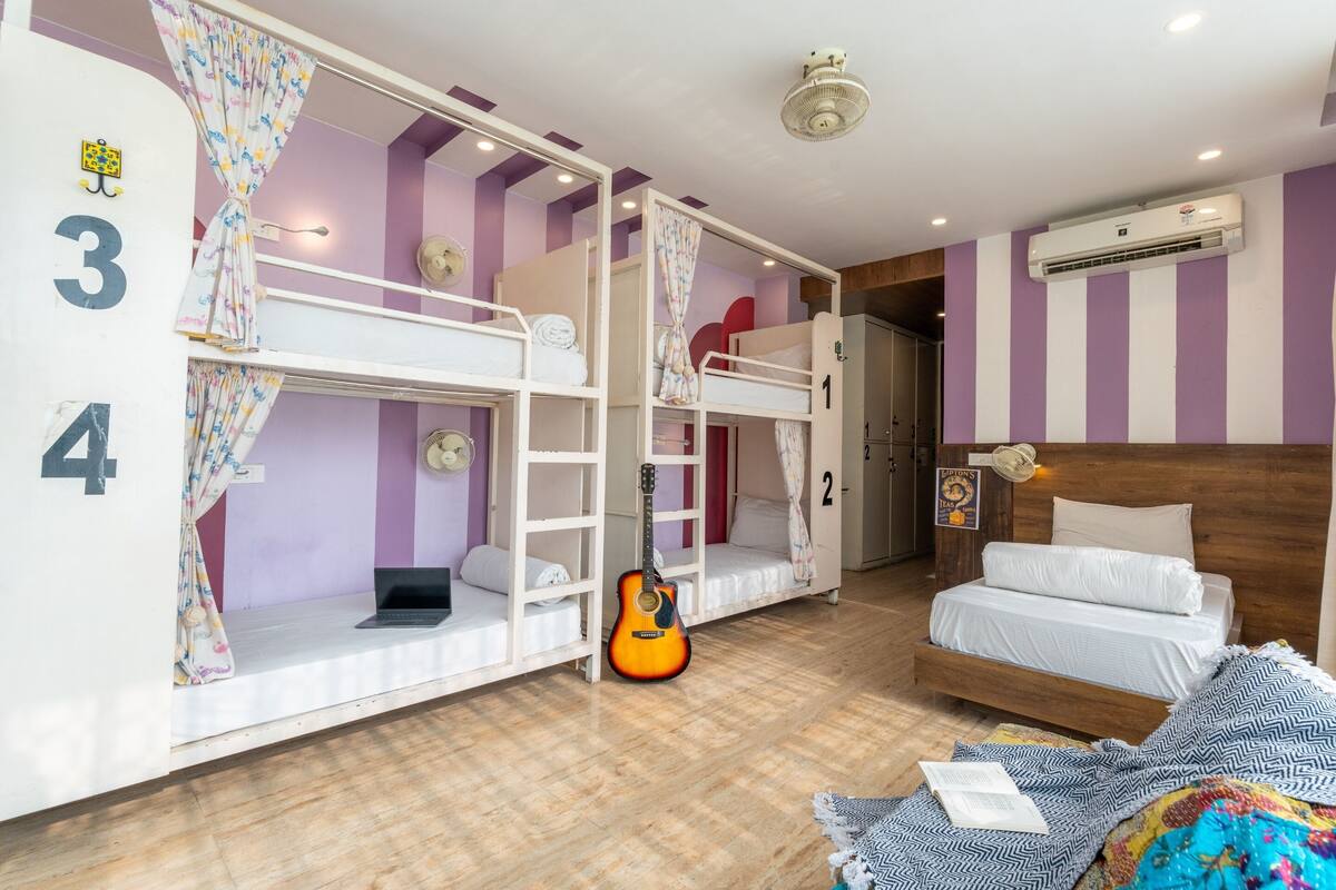 A room with bunk beds, a guitar, a laptop, and a bed with a patterned blanket.