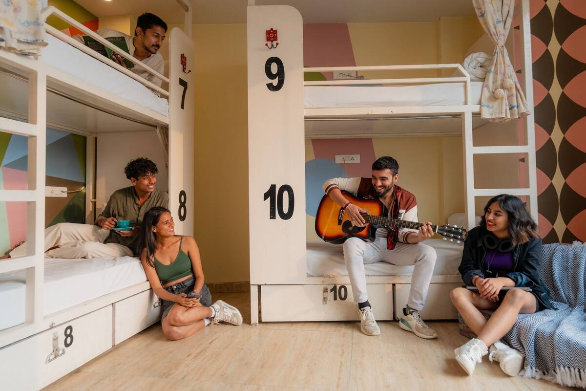 A dormitory room with bunk beds numbered 7 to 10, a sofa, and a person playing a guitar.