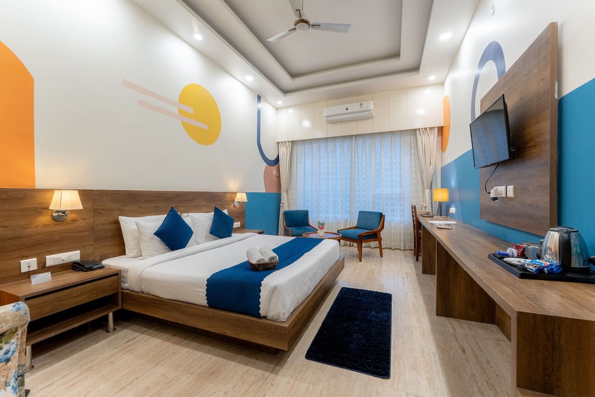 A hotel room with a bed, bedside tables, a desk, a chair, and a TV mounted on the wall.