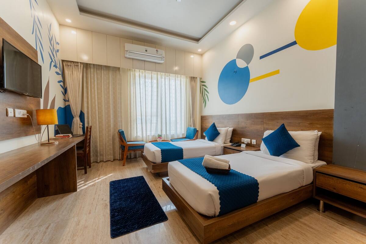 A modern hotel room with two beds, a desk with a TV, and a large window with curtains.