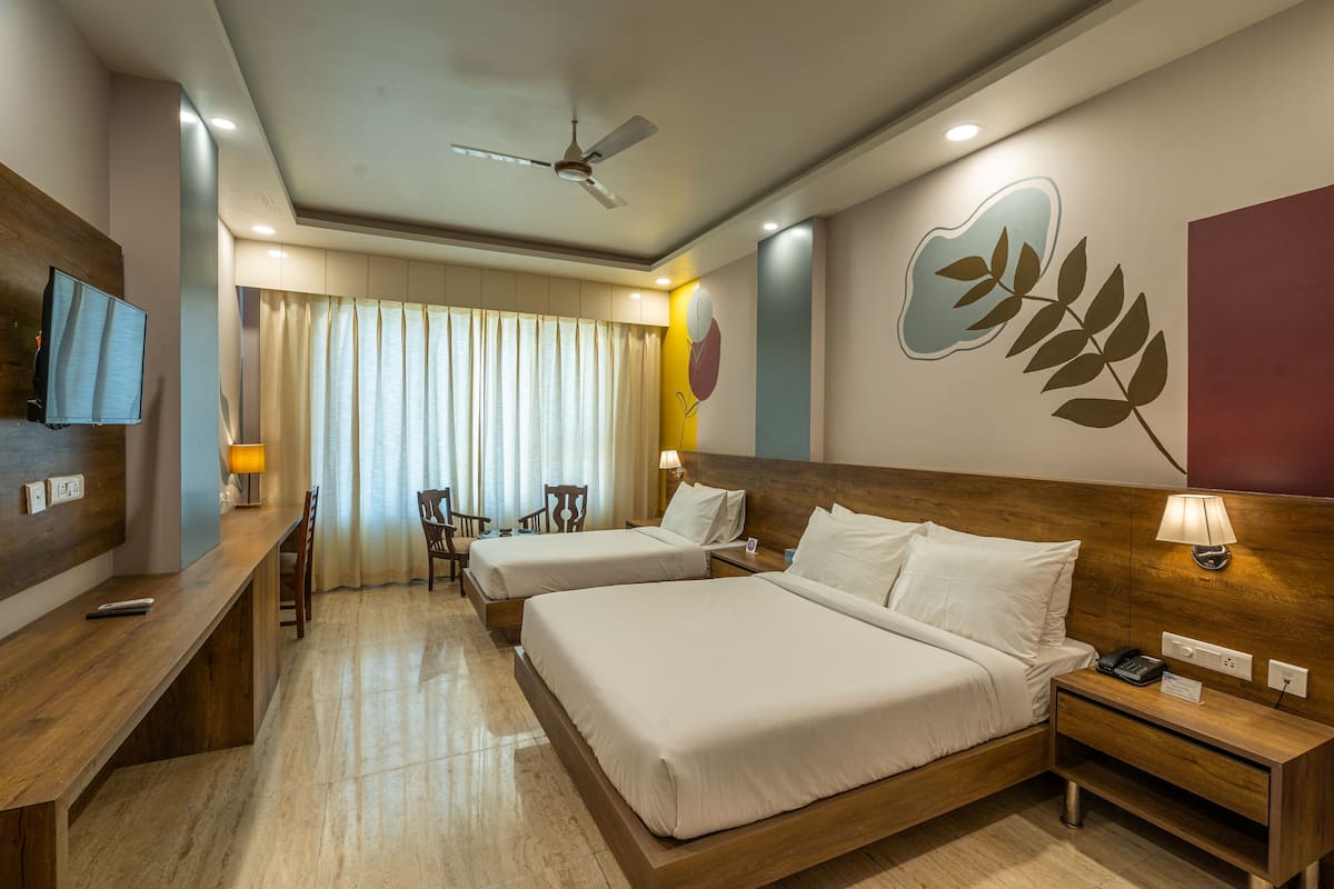A hotel room with two beds, a desk, a chair, a TV, and a ceiling fan.