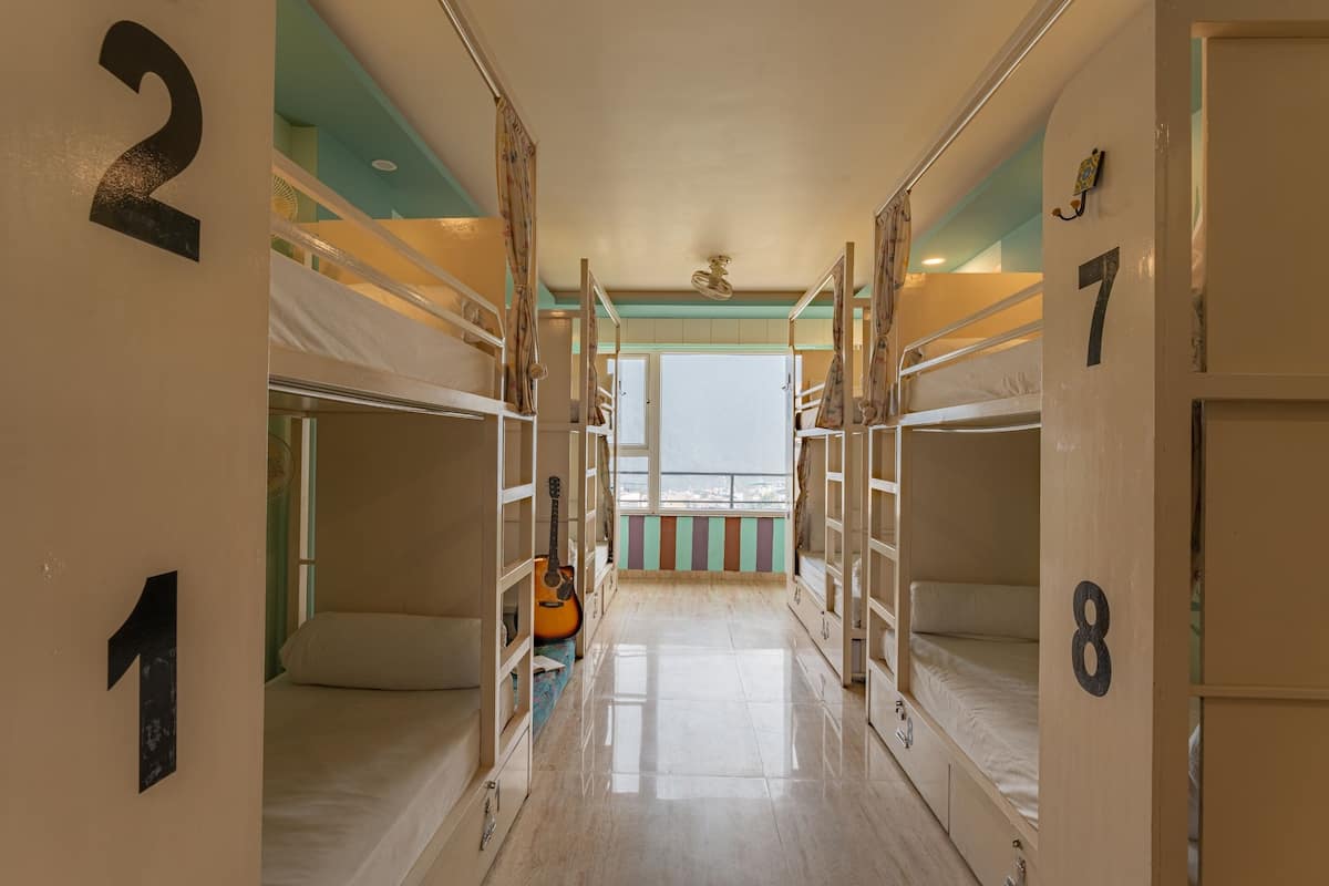 A corridor with bunk beds numbered 1 to 8, a guitar, and a window with a view.