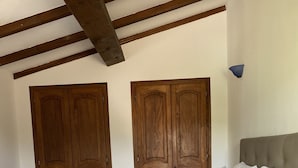 Ein ordentlich bezogenes Bett mit weißen Kissen und einer grauen, strukturierten Bettdecke in einem Zimmer mit Holztüren und einer blauen Wandleuchte.