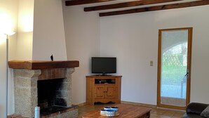 Ein Essbereich mit Kamin aus Stein, Holzbalken, einem Fernseher und einer Couch.