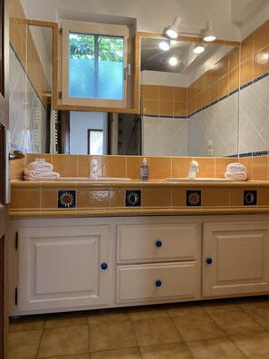 A bathroom with a tiled backsplash, a sink with a mirror above, and a window with a view of greenery.
