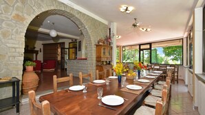 A dining area with a long wooden table set for six, stone walls, and a view through large windows.