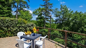 A patio with a table and chairs, surrounded by lush greenery and a clear blue sky.