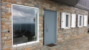 A stone facade with a large glass window, a grey door, and white shutters. - Blue Harmony (Korasida)