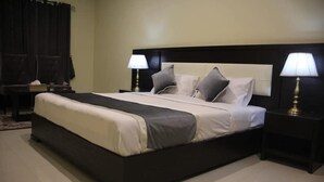 A neatly made bed with a dark headboard, two bedside lamps, and a small bedside table with a lamp. - Marjan Hotel (Rawalakot)