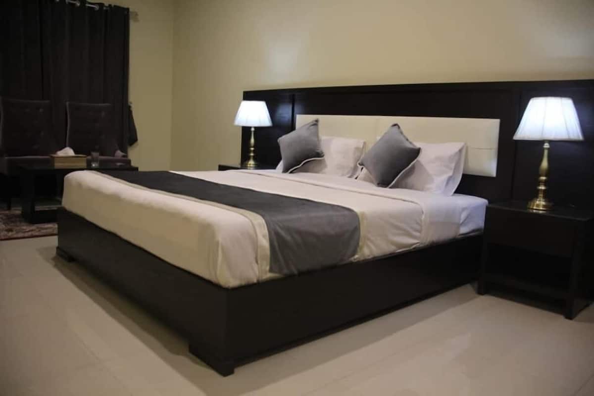 A neatly made bed with a dark headboard, two bedside lamps, and a small bedside table with a lamp.
