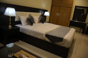A neatly made bed with a black headboard, two bedside lamps, and a wooden wardrobe in a hotel room. - Marjan Hotel (Rawalakot)