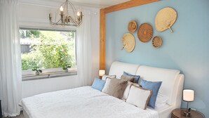 A bedroom with a large bed, a window with curtains, a chandelier, and wall decor.