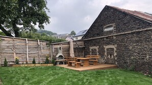 A rustic outdoor patio with a stone wall, wooden fence, and a grassy lawn.
