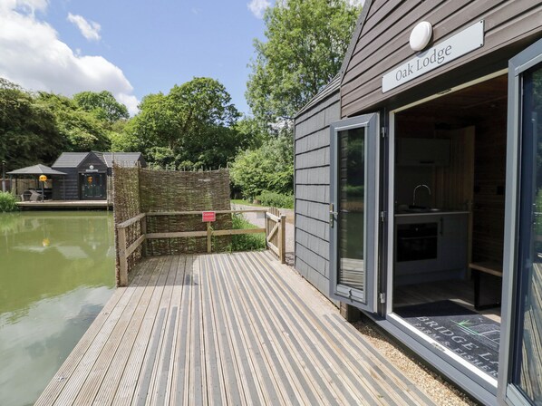 Een houten steiger die leidt naar een chalet met een bord waarop 'Oak Lodge' staat.