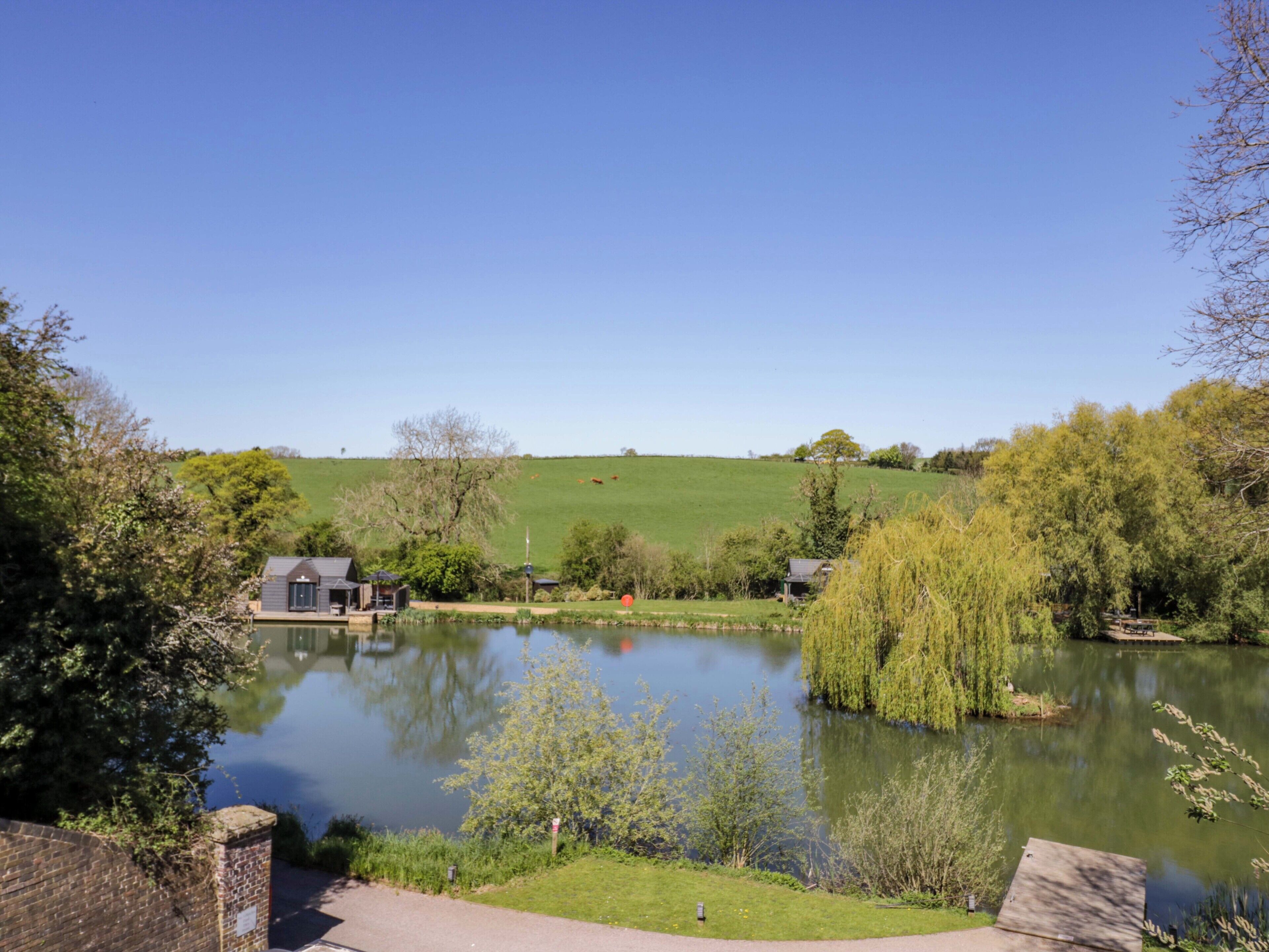 A serene lakeside view with a small house, a pond, and surrounding greenery.