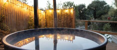 Un bain à remous avec une terrasse en bois et une clôture en bambou en arrière-plan.