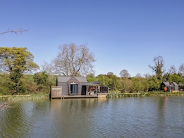 Una cabaña junto al lago con un muelle, un espacio de estar al aire libre techado y una pequeña terraza.